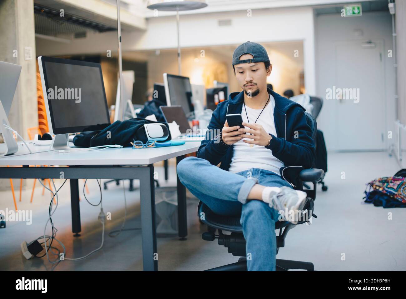 Programmeur d'ordinateur masculin utilisant un smartphone assis sur une chaise au bureau Banque D'Images
