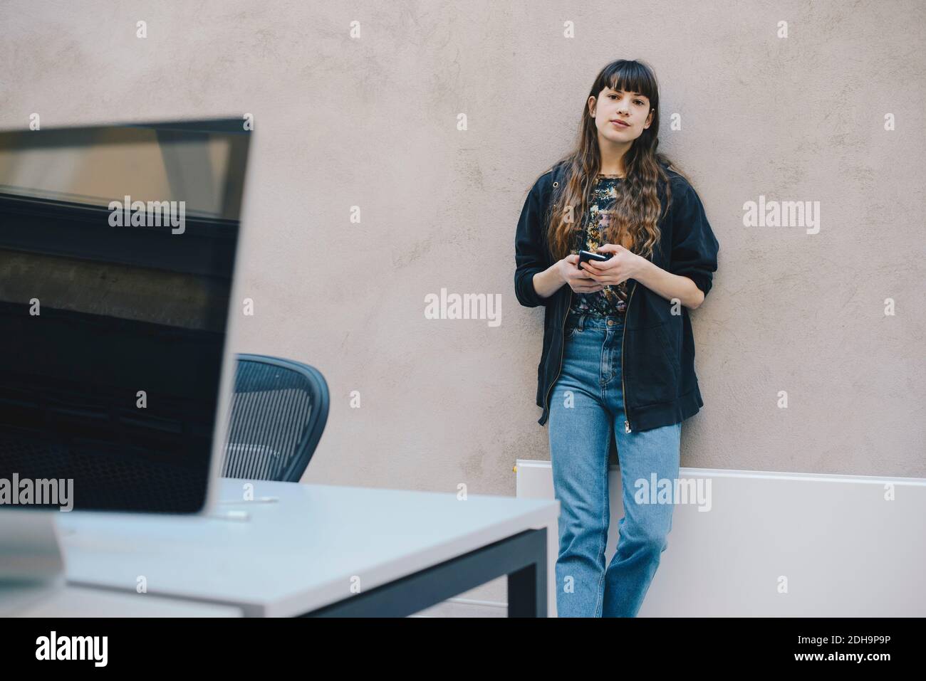 Portrait d'une femme programmeur tenant un smartphone debout contre le mur beige dans le bureau Banque D'Images