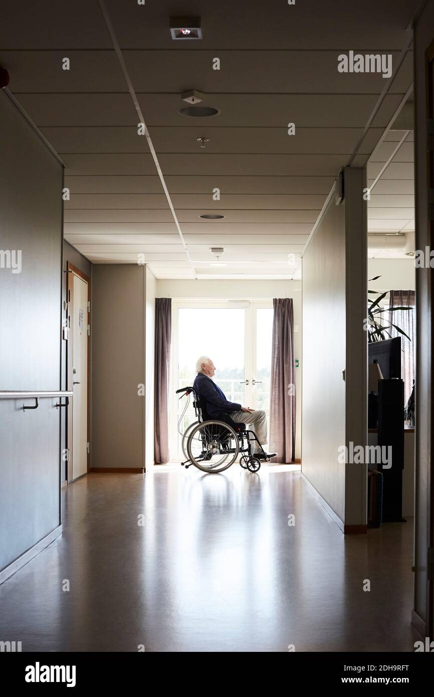 Vue latérale d'un homme âgé assis en fauteuil roulant à couloir de l'hôpital Banque D'Images