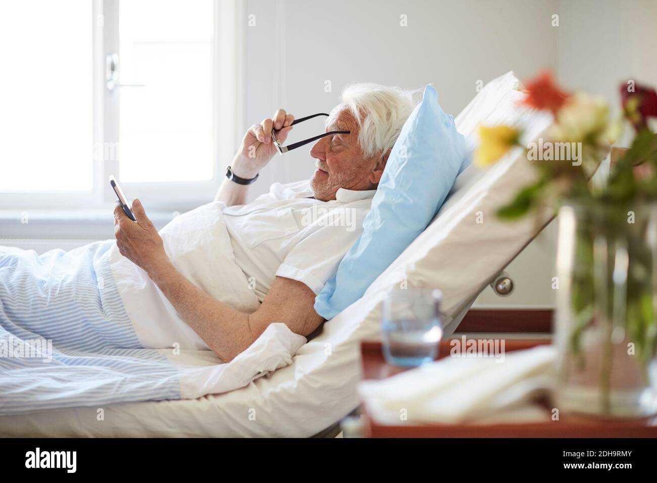 Vue latérale d'un homme âgé portant des lunettes de vue tout en utilisant Smart téléphone dans le service hospitalier Banque D'Images