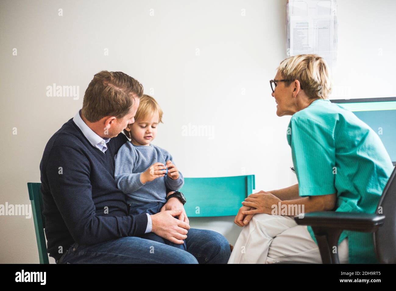 Vue latérale d'une femme mature médecin parlant à un garçon avec père en clinique Banque D'Images