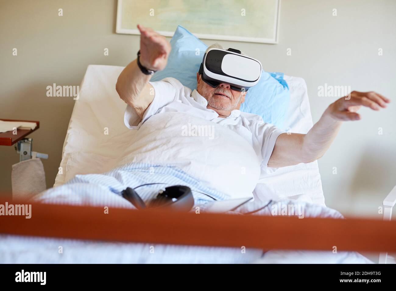 Niveau de surface de l'homme âgé avec les bras relevés à l'aide de VR des lunettes sur le lit dans le service hospitalier Banque D'Images