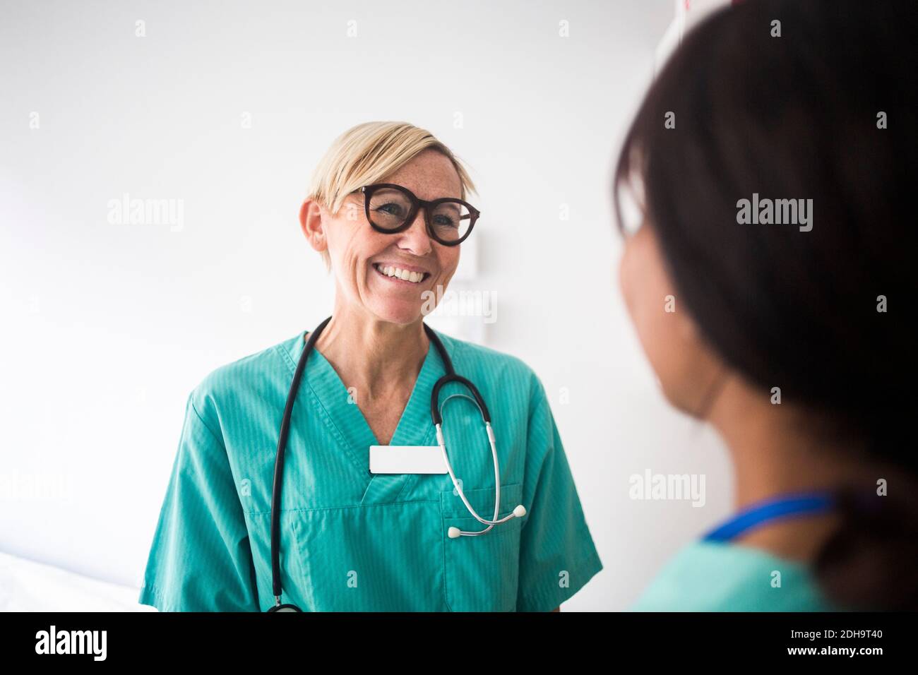 Un pédiatre mûr souriant s'est adressé à une collègue tout en restant debout clinique Banque D'Images