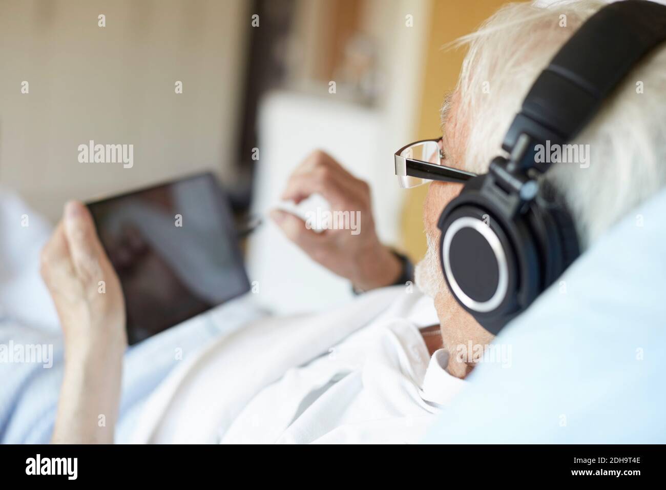 Vue sur l'épaule d'un homme âgé portant un casque pendant utilisation d'une tablette numérique à l'hôpital Banque D'Images