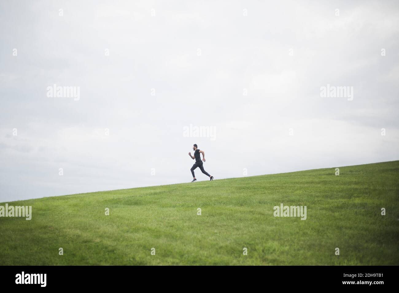 Vue latérale d'un jeune homme en train de courir sur le terrain contre le ciel nuageux ciel Banque D'Images