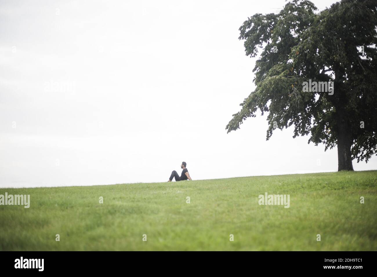 Vue à mi-distance de l'homme assis sur un terrain herbeux contre ciel Banque D'Images