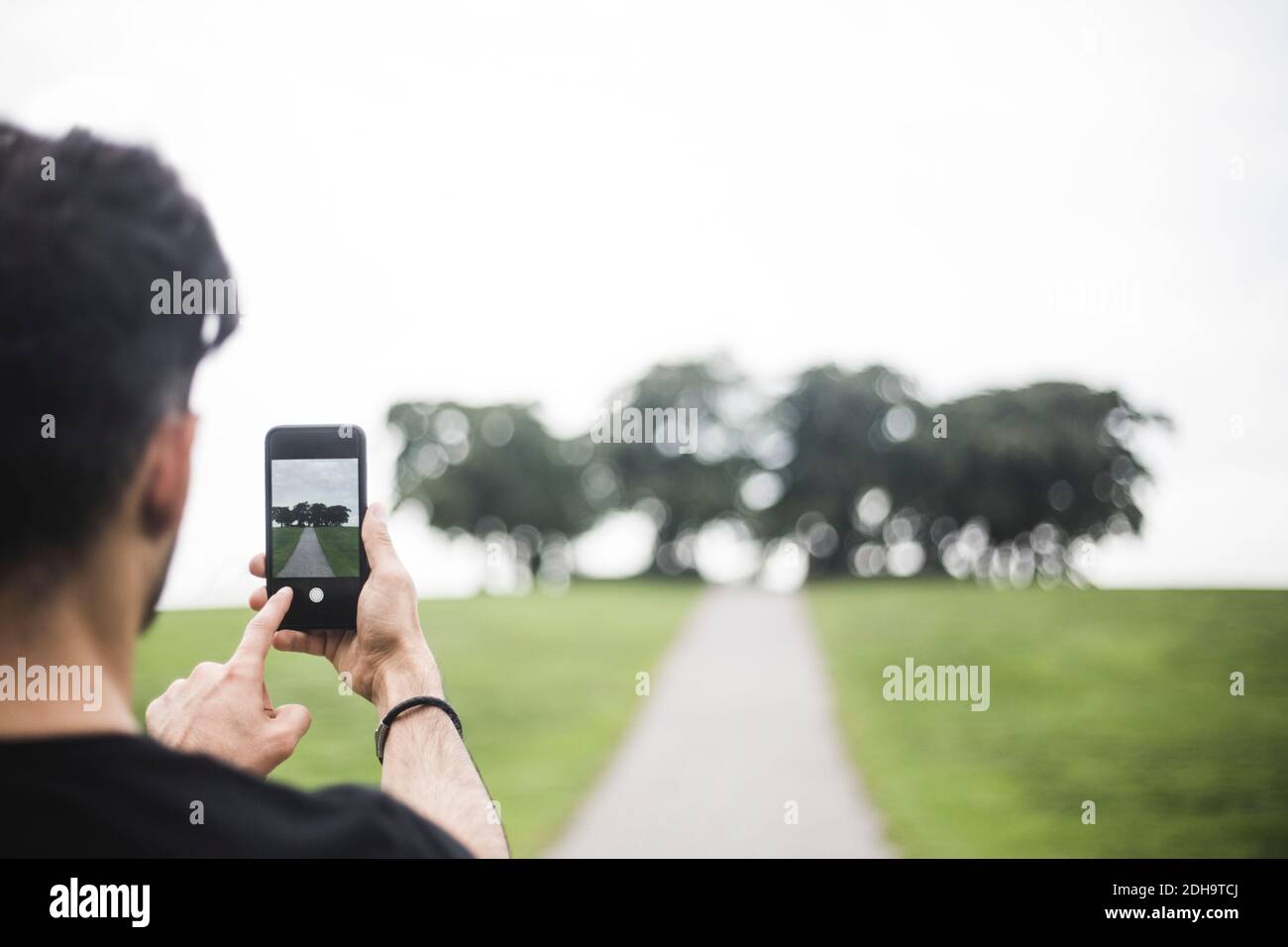Vue arrière d'un jeune homme qui photographie avec un smartphone contre ciel Banque D'Images