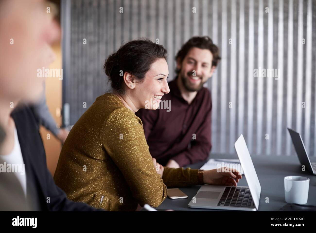 Une équipe d'affaires créative souriante assise avec un ordinateur portable à la table de conférence dans la salle de conseil Banque D'Images