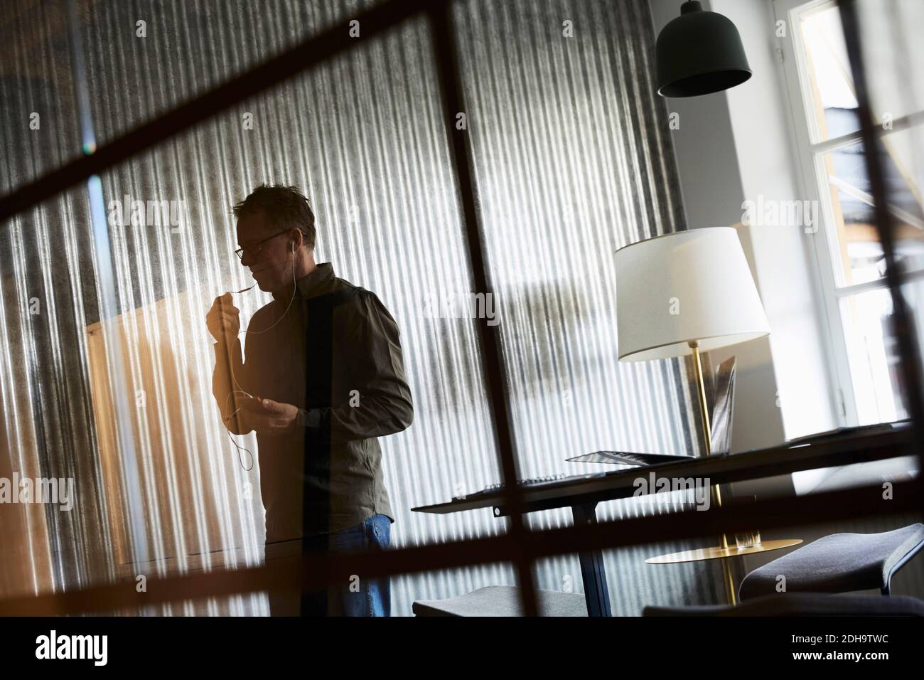 Photo d'un homme d'affaires parlant sur un smartphone via un casque vue depuis le verre au bureau créatif Banque D'Images