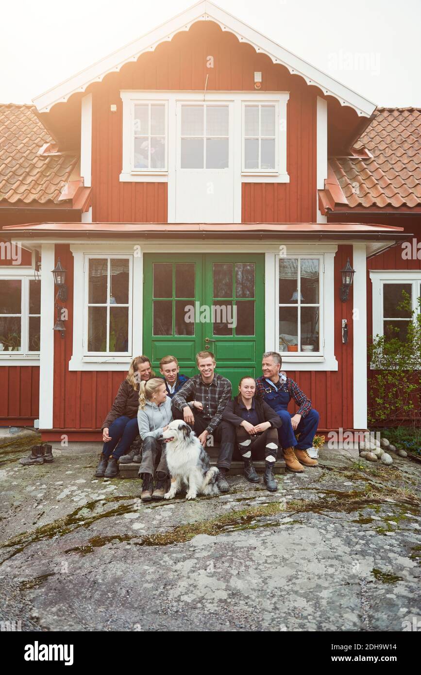 Famille souriante assise avec un animal de compagnie à l'entrée de la maison Banque D'Images