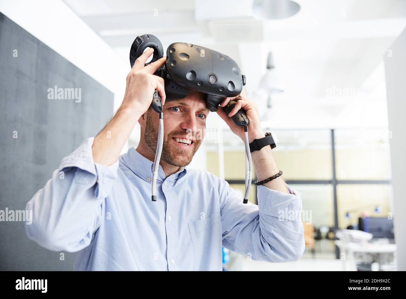 Homme d'affaires souriant portant un stimulateur de réalité virtuelle au bureau créatif Banque D'Images