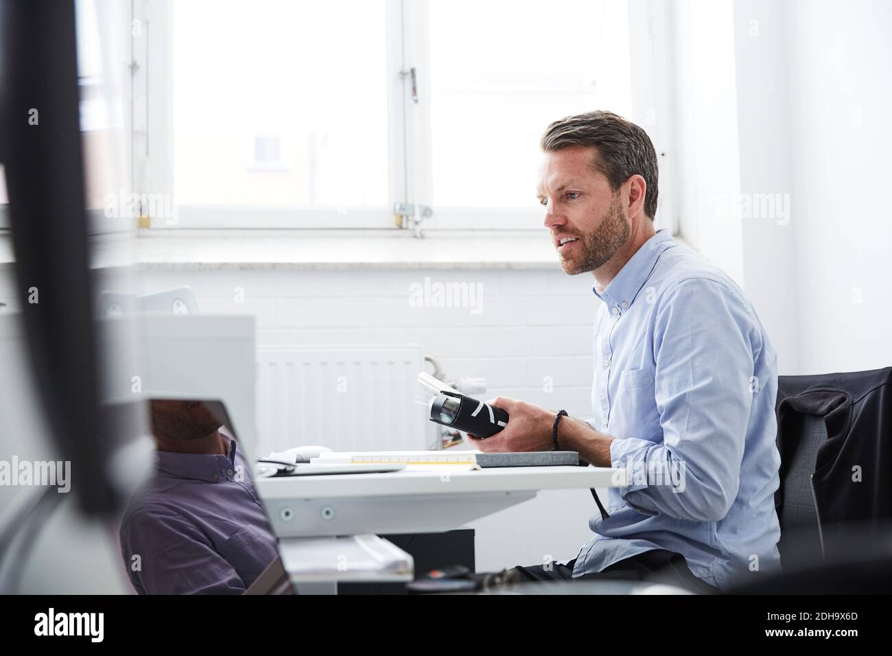Homme d'affaires avec dossier regardant l'ordinateur portable tout en restant dans la créativité bureau Banque D'Images