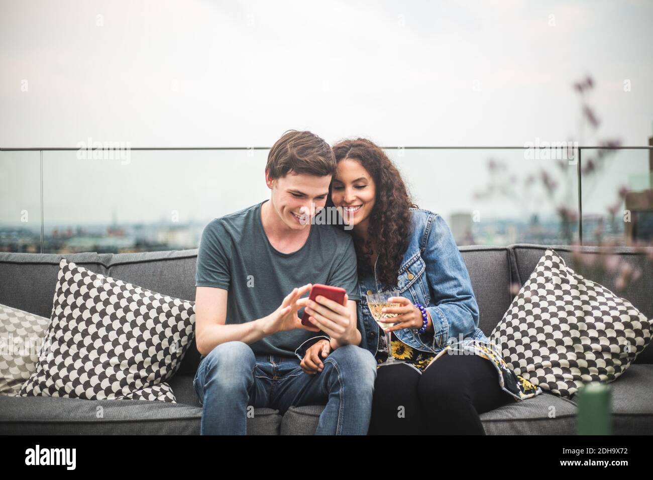 Jeune homme montrant un smartphone à une amie avec un verre sur la terrasse Banque D'Images