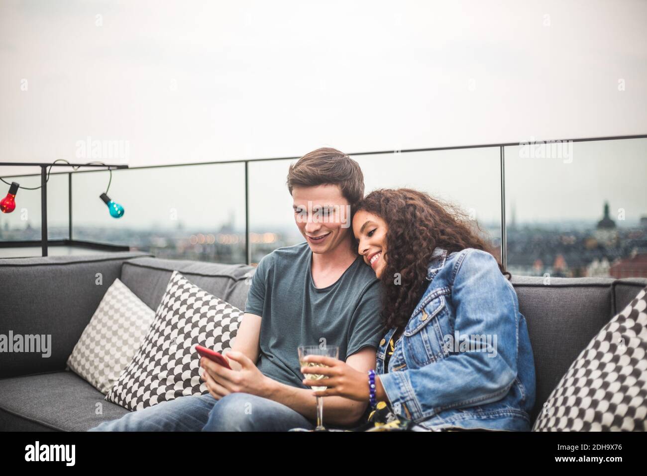 Homme souriant montrant un smartphone à une femme avec un verre sur la terrasse Banque D'Images