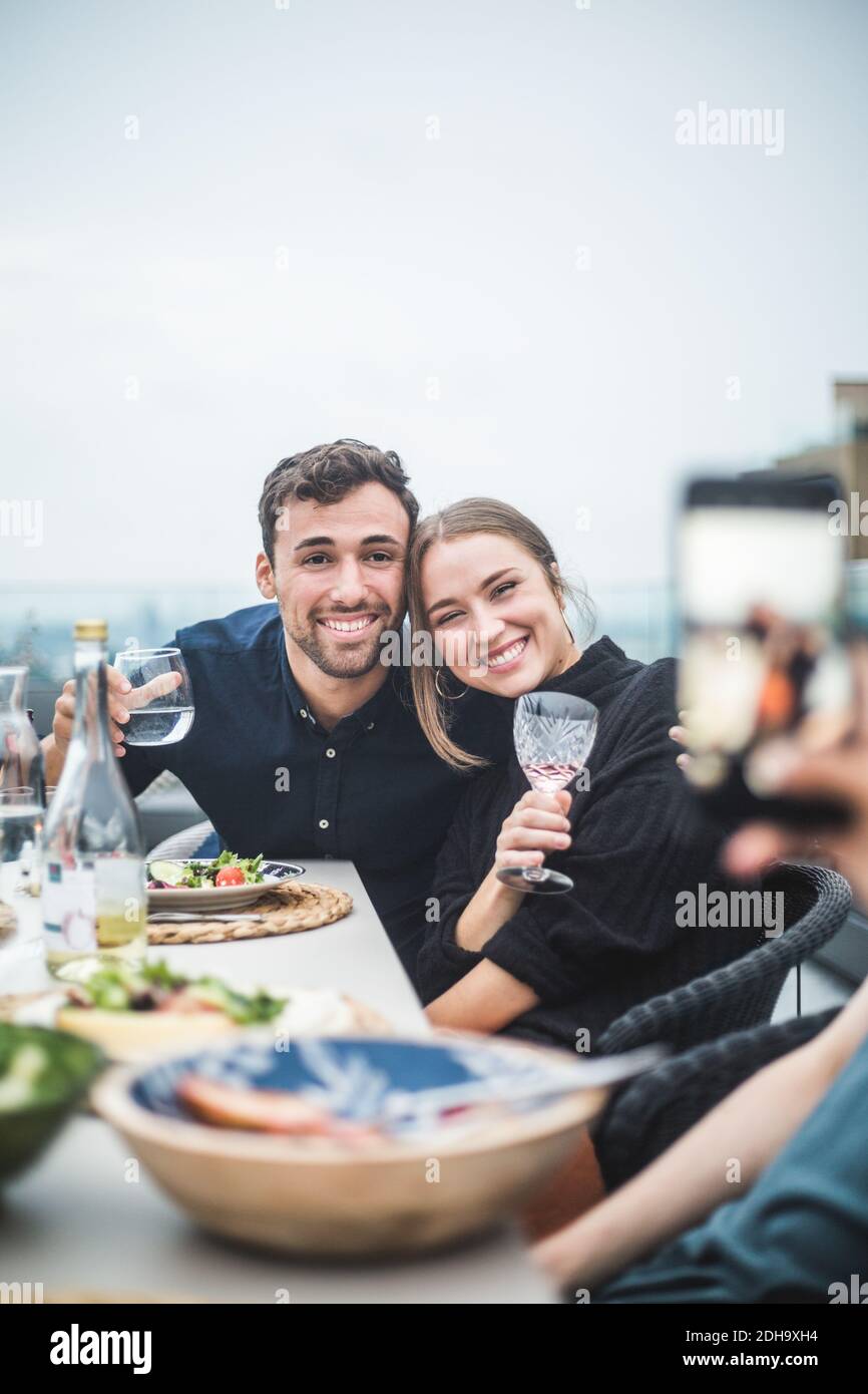 Des amis heureux avec des boissons posant pour la photographie pendant la fête sur le toit Banque D'Images