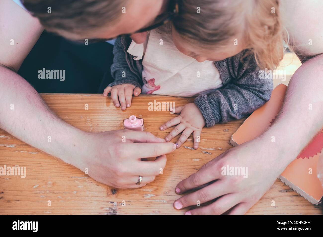 Vue en grand angle du père qui peint les ongles de sa fille à la table à l'extérieur Banque D'Images