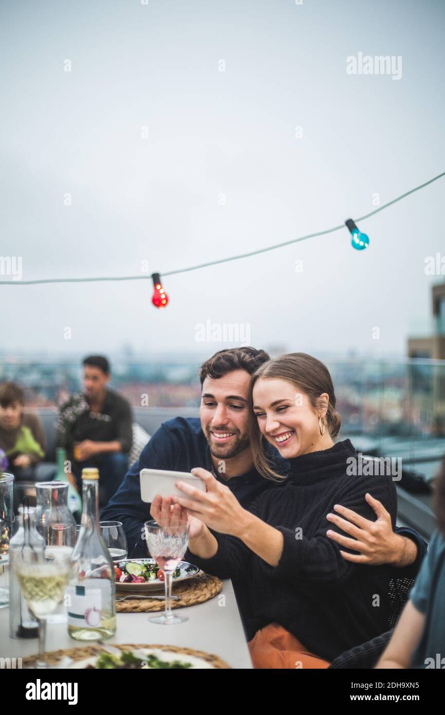 Des amis heureux avec des boissons prenant le selfie par le biais de smartphone pendant fête sur le toit Banque D'Images
