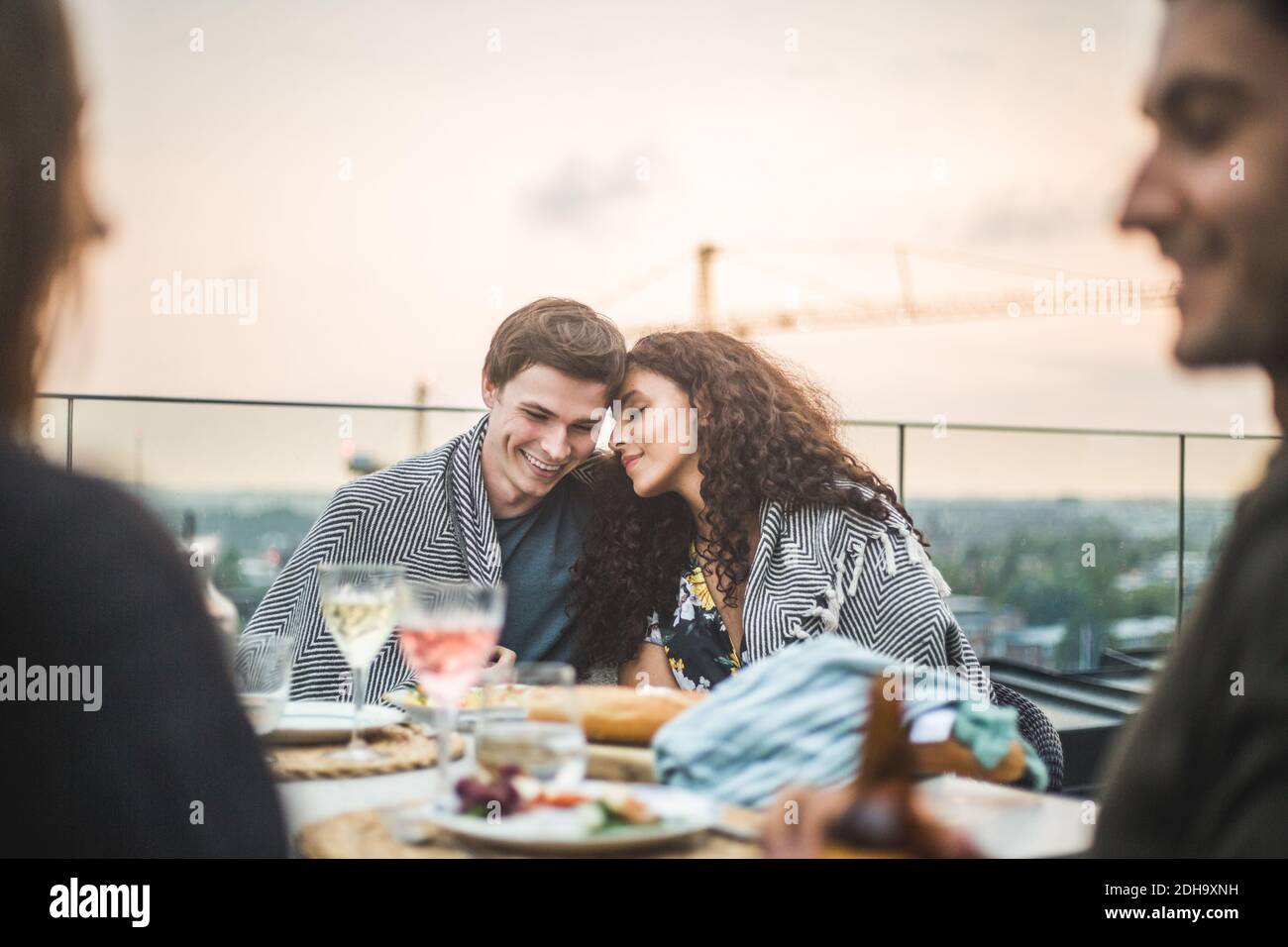Souriant homme et femme assis avec une couverture sur la terrasse pendant coucher de soleil Banque D'Images