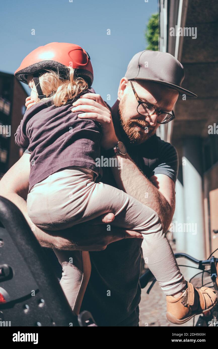 Père mettant une fille sur le siège arrière de vélo à l'extérieur Banque D'Images