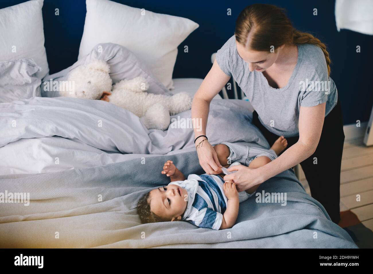 Mère habillant bébé garçon sur le lit à la maison Banque D'Images
