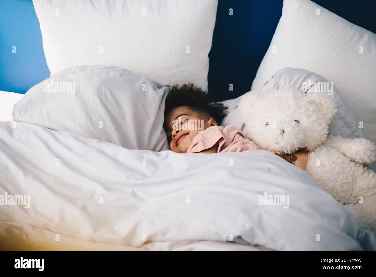 Garçon souriant dormant avec un ours en peluche sur le lit à la maison Banque D'Images