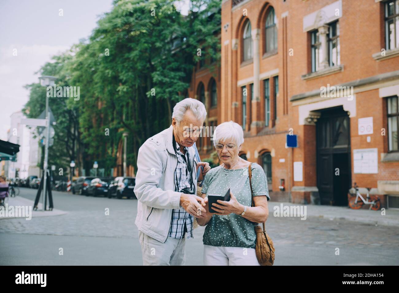 Femme senior tenant un smartphone discutant avec un partenaire tout en explorant en ville Banque D'Images