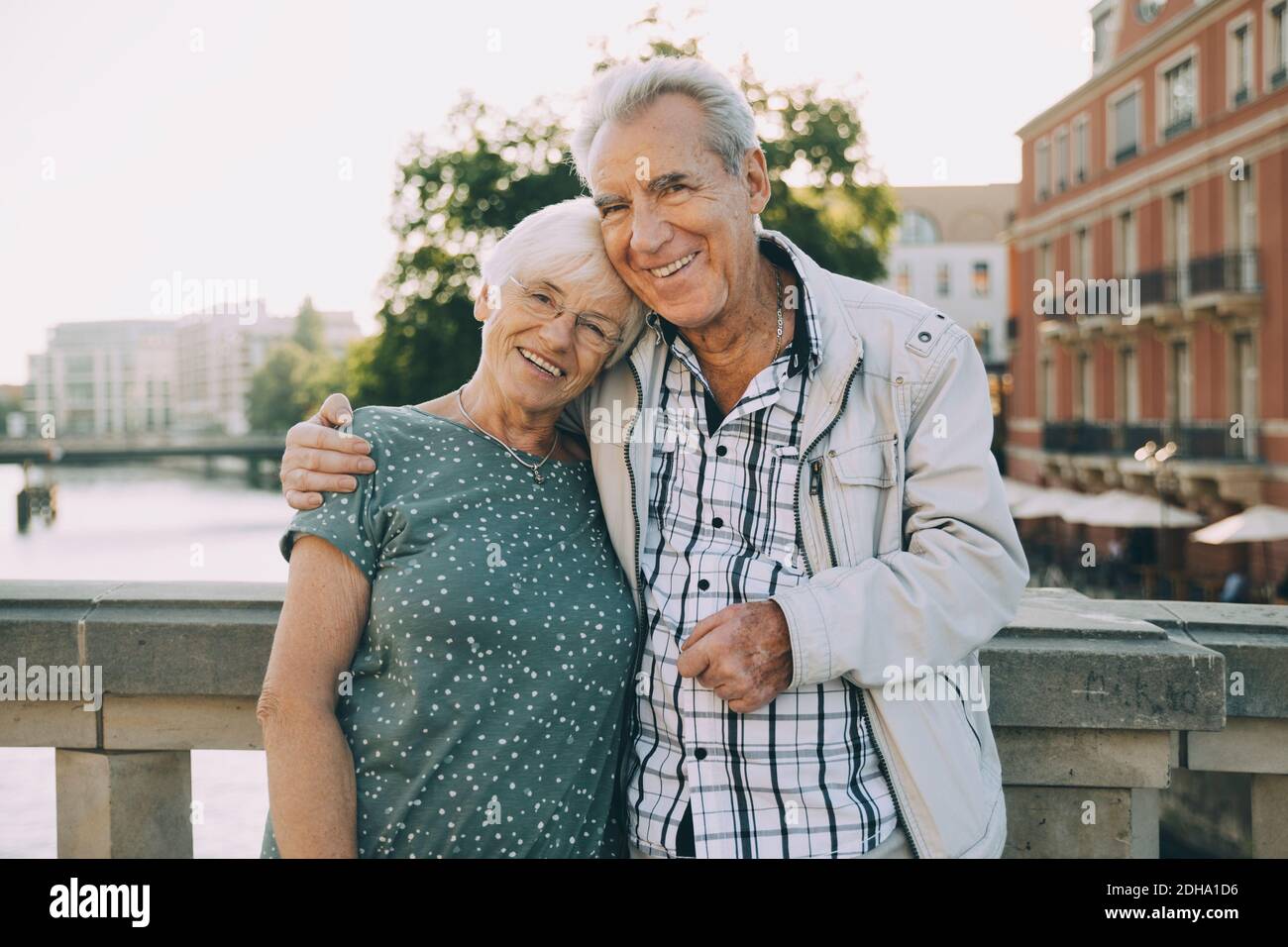 Portrait d'un homme âgé souriant autour du bras, debout avec son partenaire contre la rambarde en ville Banque D'Images