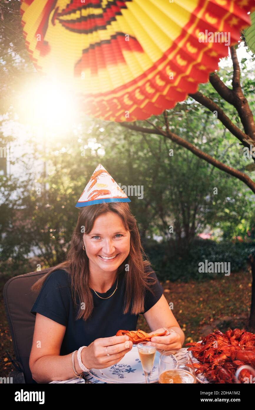 Portrait d'une femme mûre heureuse mangeant de l'écrevisse tout en étant assise table à manger pendant la fête dans le jardin Banque D'Images