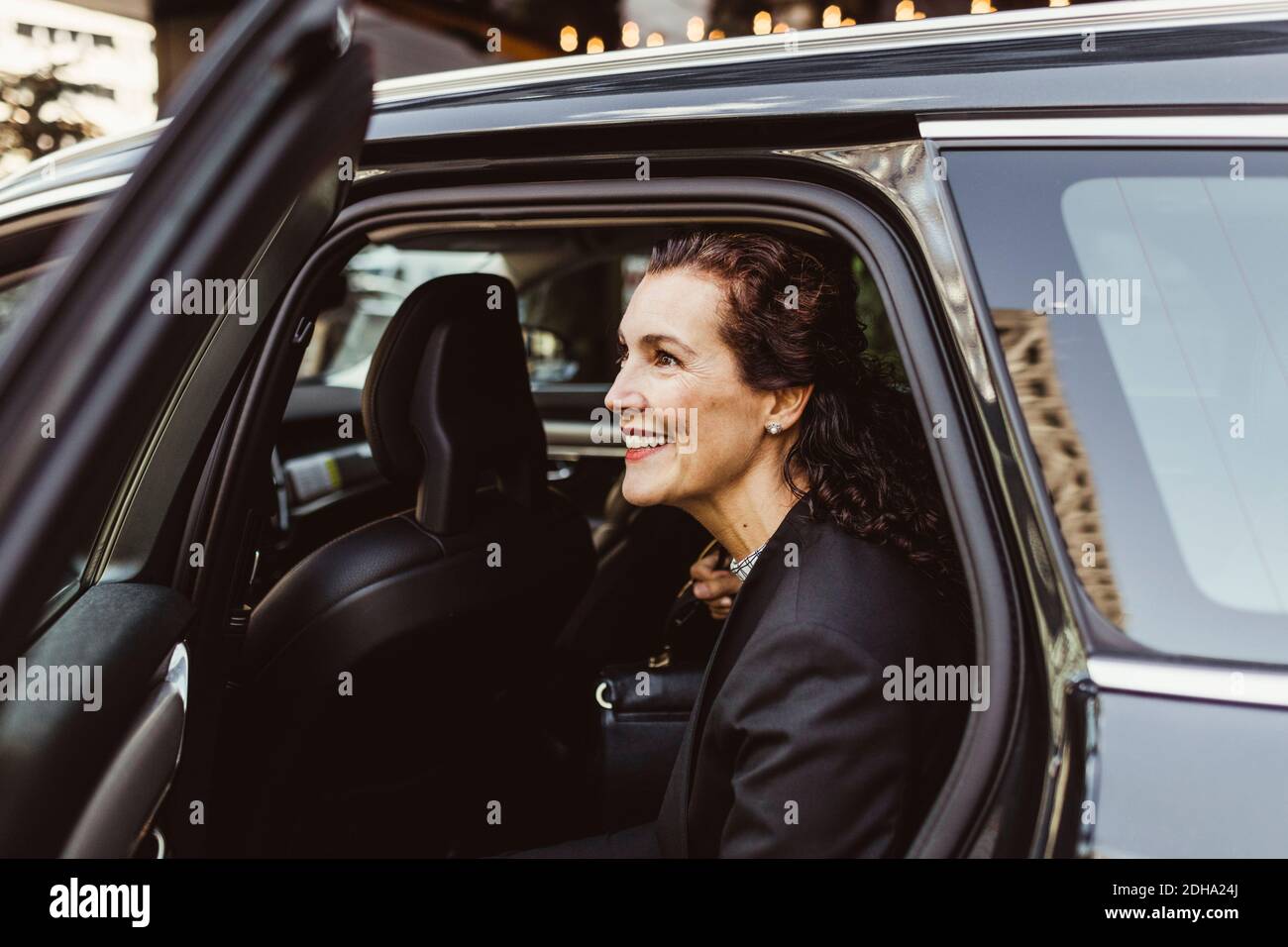 Femme entrepreneur souriante qui regarde loin en sortant de la voiture Banque D'Images