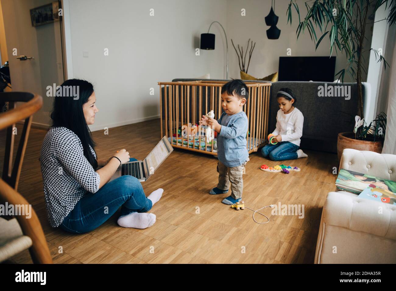 Mère utilisant un ordinateur portable tout en travaillant à la maison assis avec des enfants dans la salle de séjour Banque D'Images