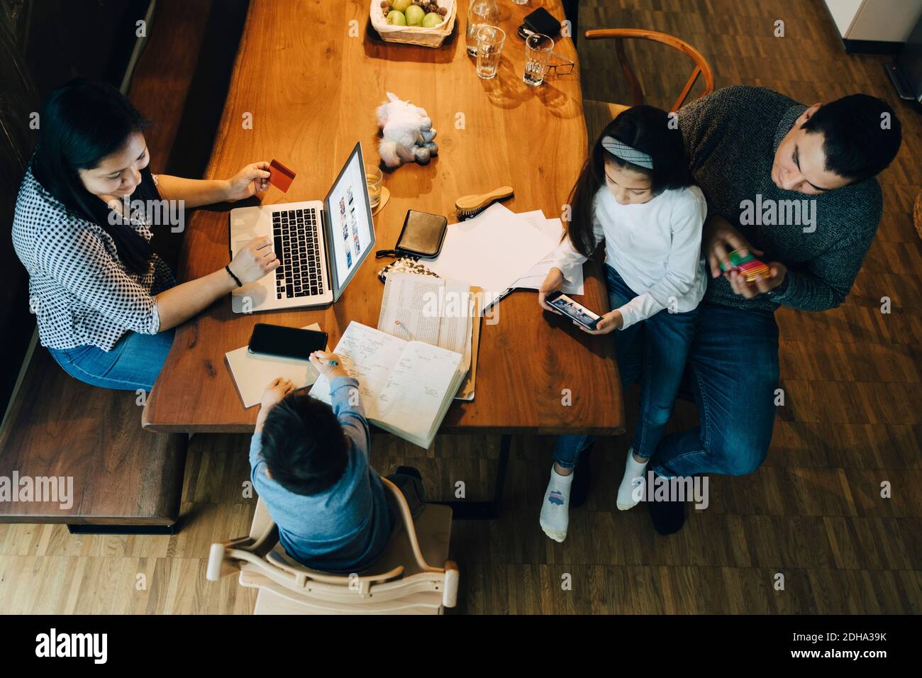 Vue en grand angle de la mère à l'aide d'un ordinateur portable à la table père assis avec des enfants dans la salle de séjour Banque D'Images