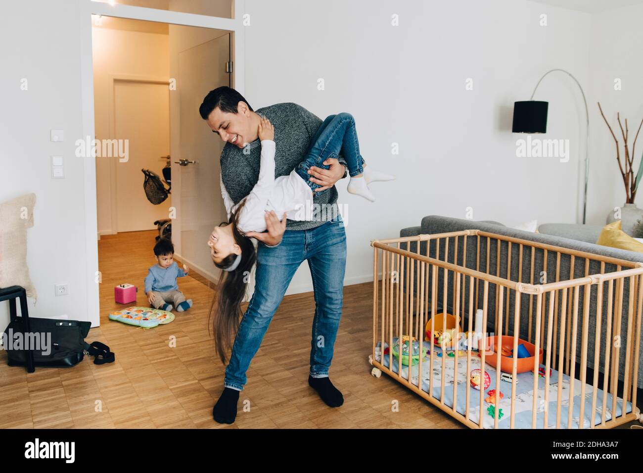 Pleine longueur de père joueur soulevant sa fille pendant son fils jouer avec des jouets dans la salle de séjour Banque D'Images