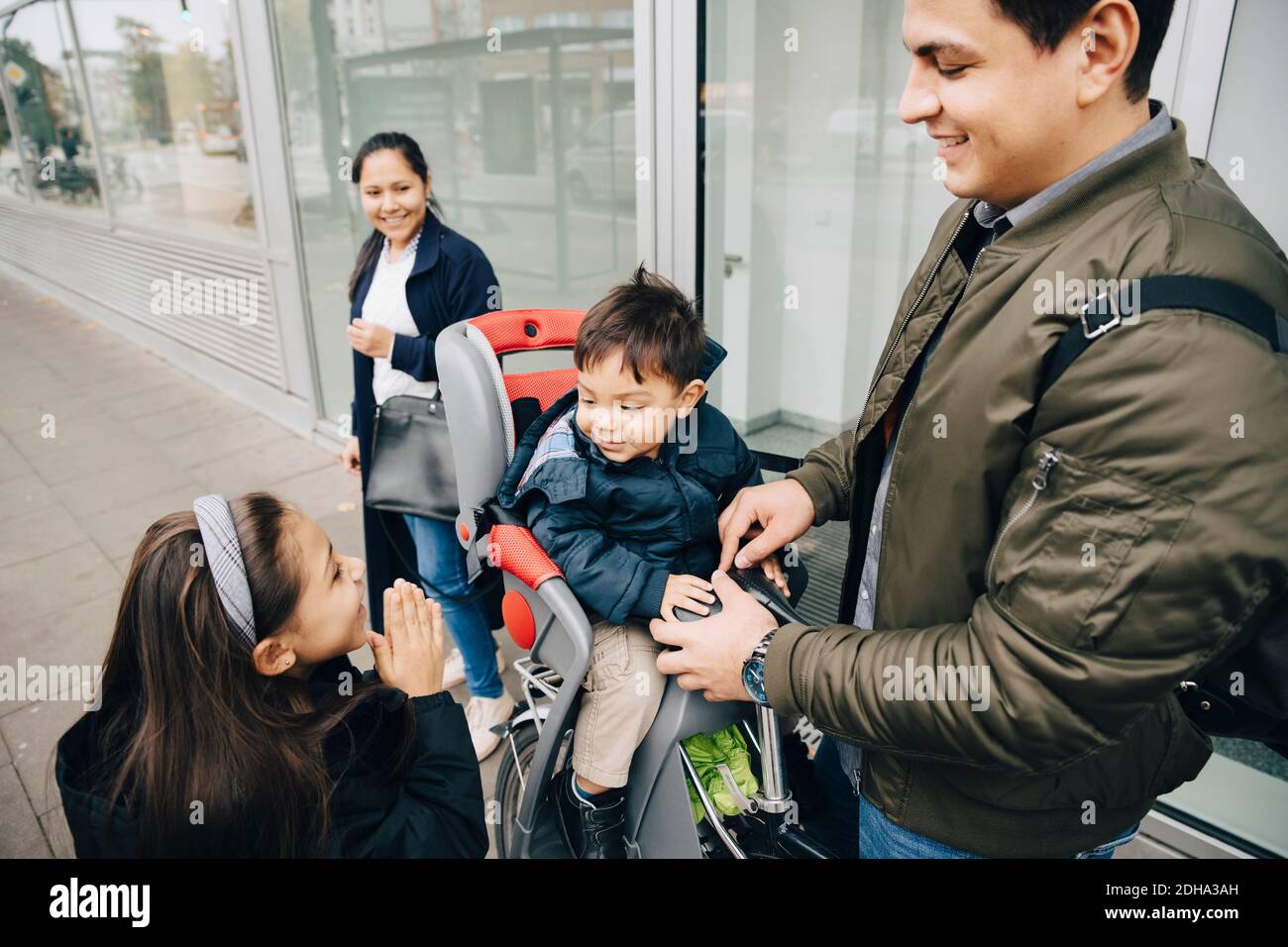Sœur souriante regardant son frère assis à vélo avec ses parents en ville Banque D'Images
