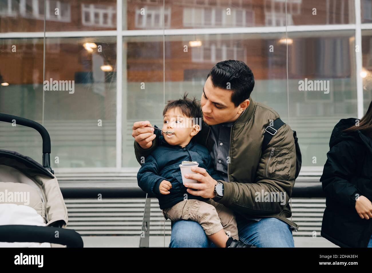 Père nourrissant bébé à son fils pendant qu'il est assis dans le bus arrêt en ville Banque D'Images