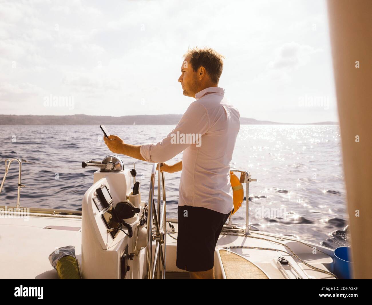 Vue latérale d'un homme tenant un téléphone portable pendant la navigation en catamaran sur la mer contre le ciel pendant la journée ensoleillée Banque D'Images