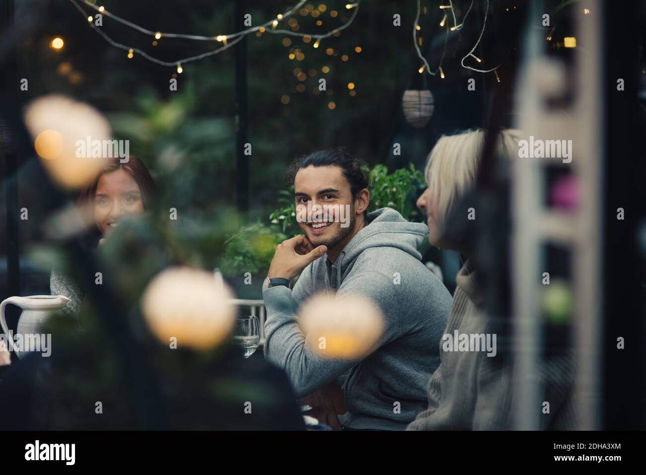 Jeune homme souriant assis parmi des amis à la table à manger jardin arrière pendant la fête du jardin Banque D'Images