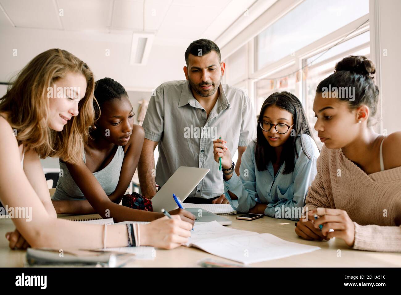 Des adolescentes étudient en classe pendant que le professeur se tient à table Banque D'Images