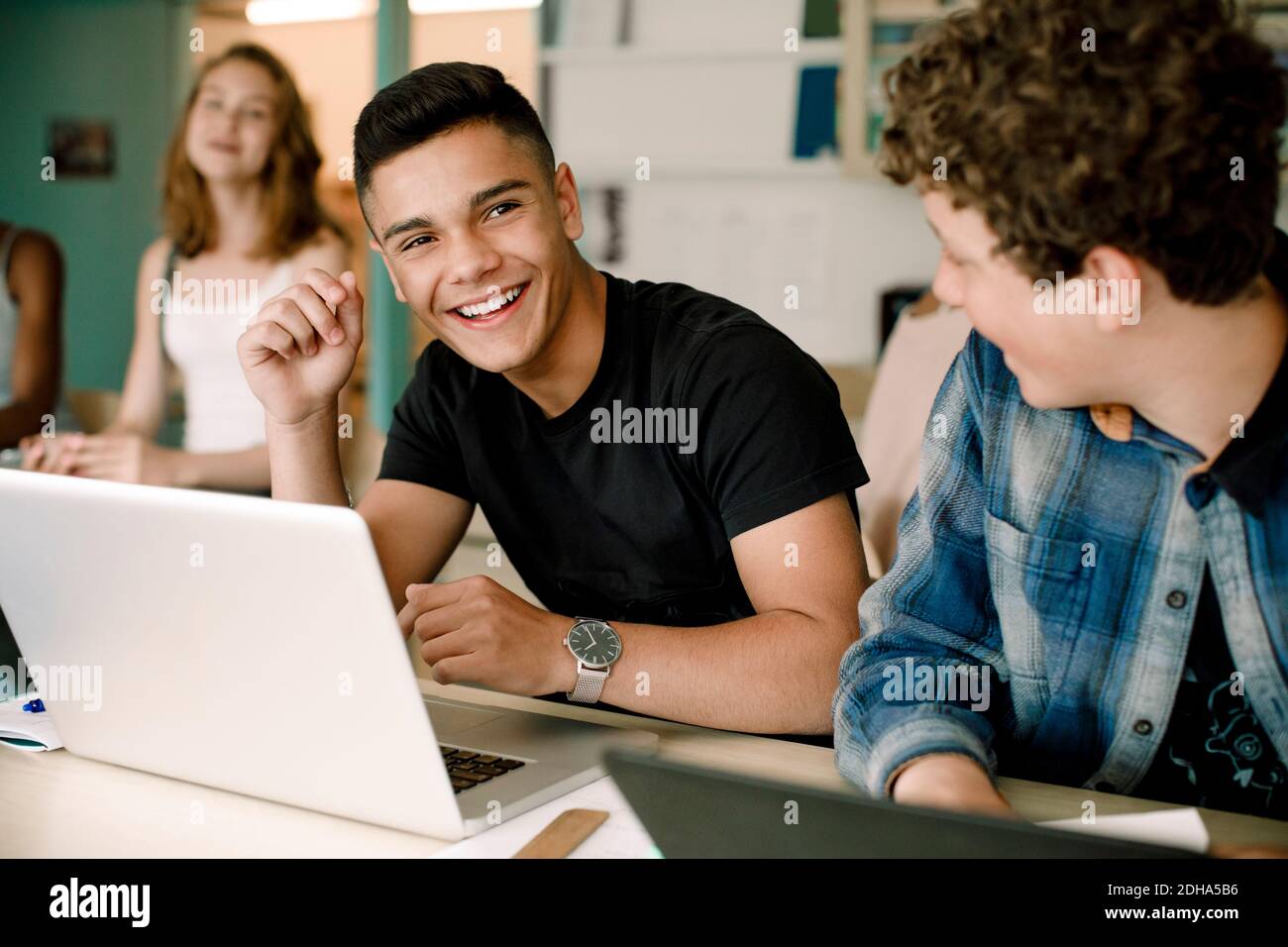 Souriant, les élèves de sexe masculin utilisent un ordinateur portable sur une table lorsqu'ils sont assis salle de classe Banque D'Images