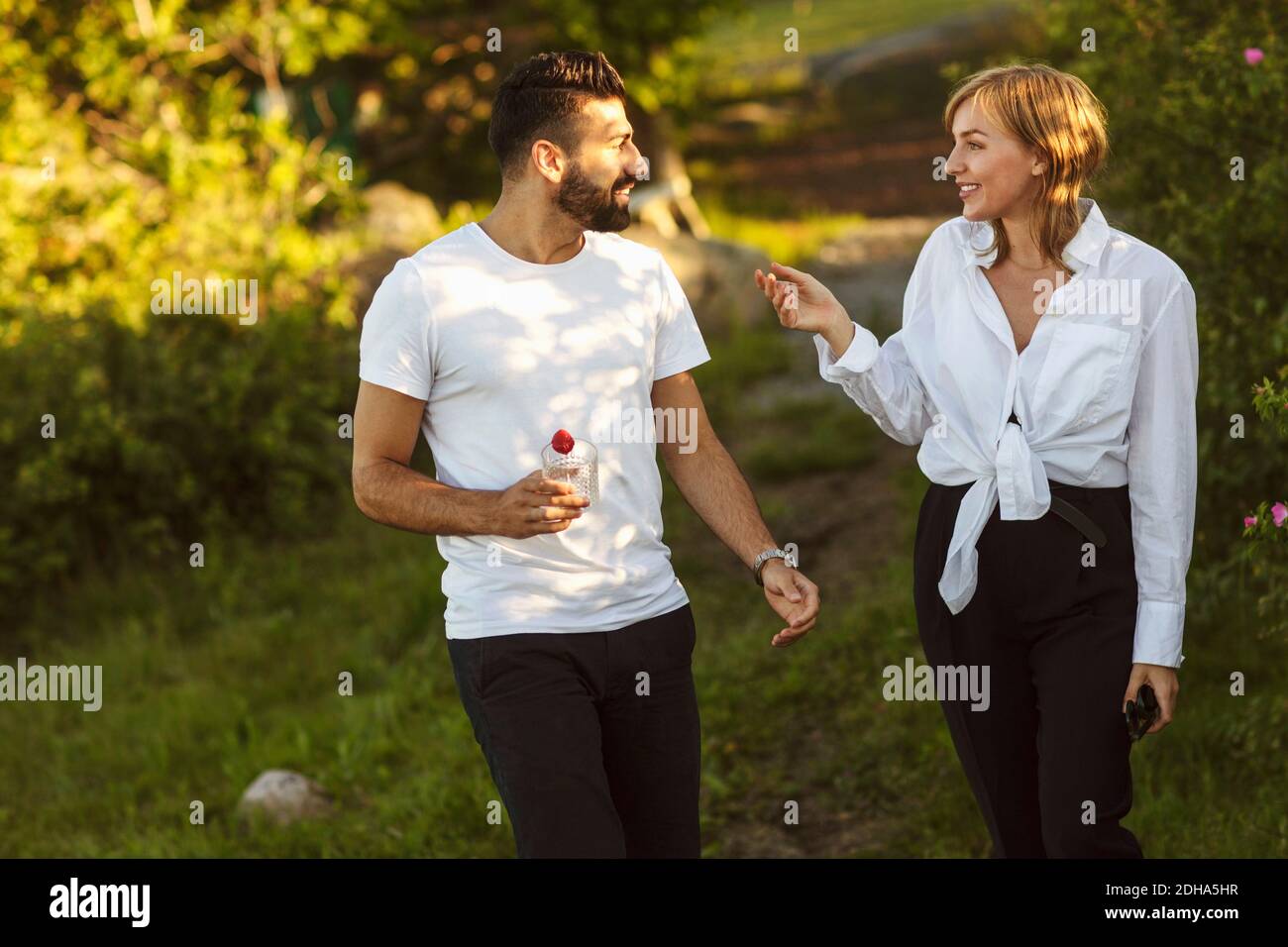 Homme et femme souriants parlant en marchant sur un terrain herbeux Banque D'Images