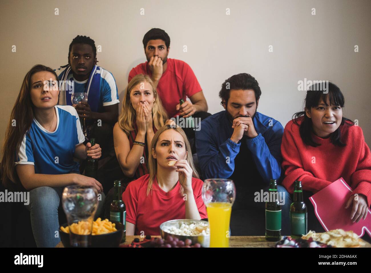 Des amis hommes et femmes inquiets regardant le sport pendant qu'ils étaient assis canapé à la maison Banque D'Images