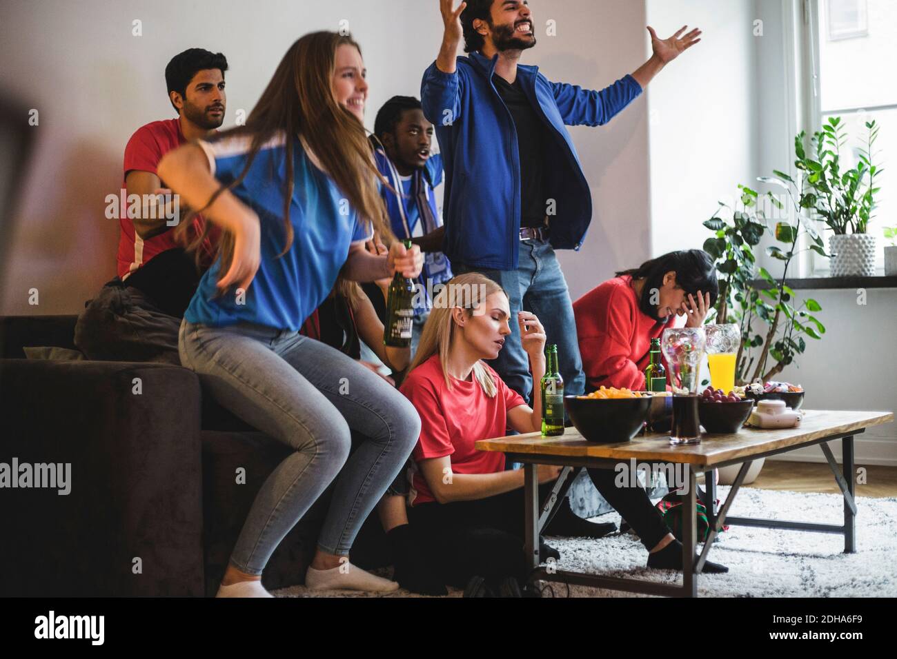 Hommes et femmes fans de football regardant le match de football en étant assis à la maison Banque D'Images