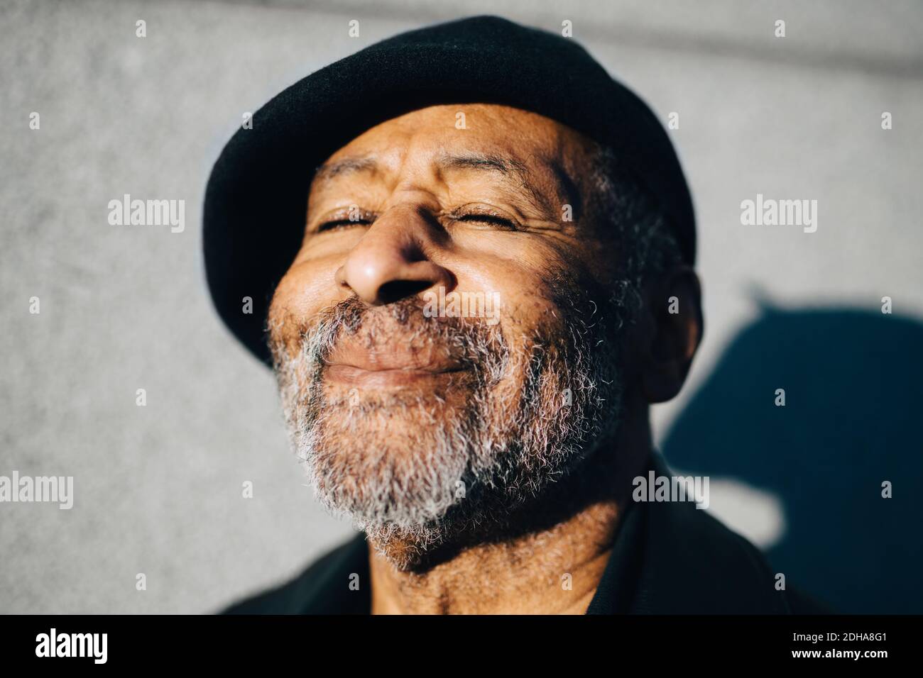 Homme âgé souriant avec les yeux fermés contre le mur Banque D'Images