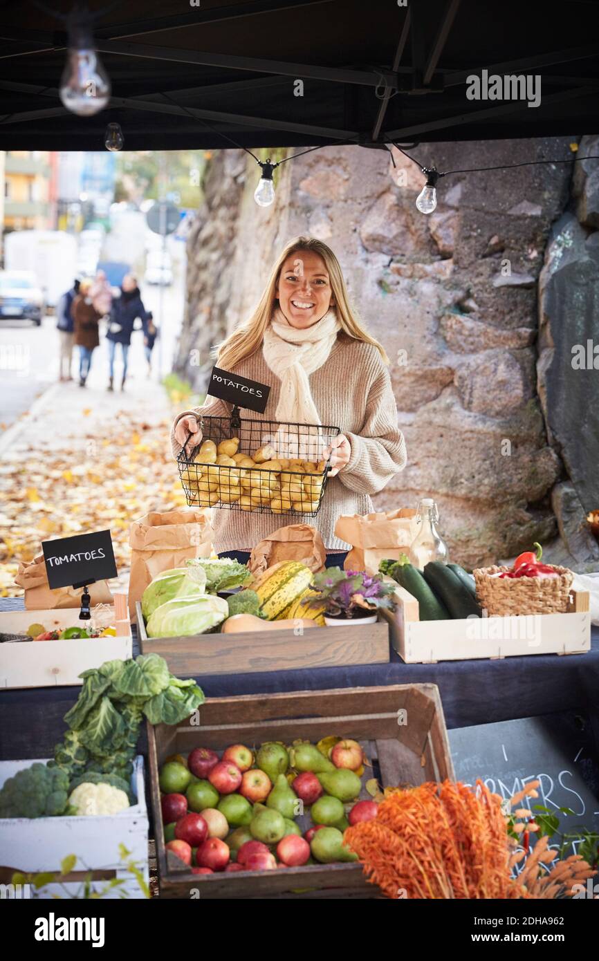 Portrait d'une femme souriante tenant un panier de pommes de terre fraîchement préparé le marché est au point mort Banque D'Images