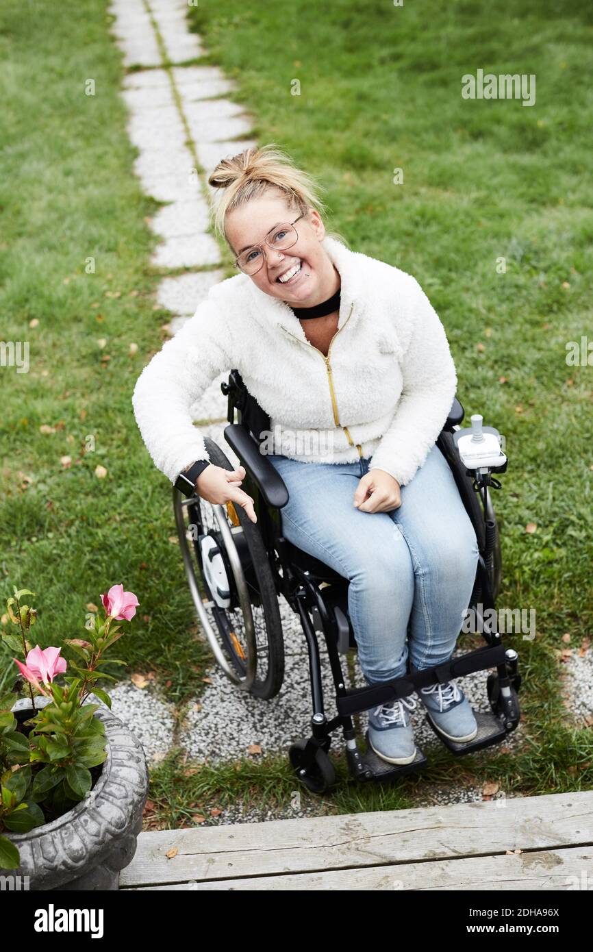 Portrait complet d'une femme handicapée souriante assise sur un fauteuil roulant dans l'arrière-cour Banque D'Images