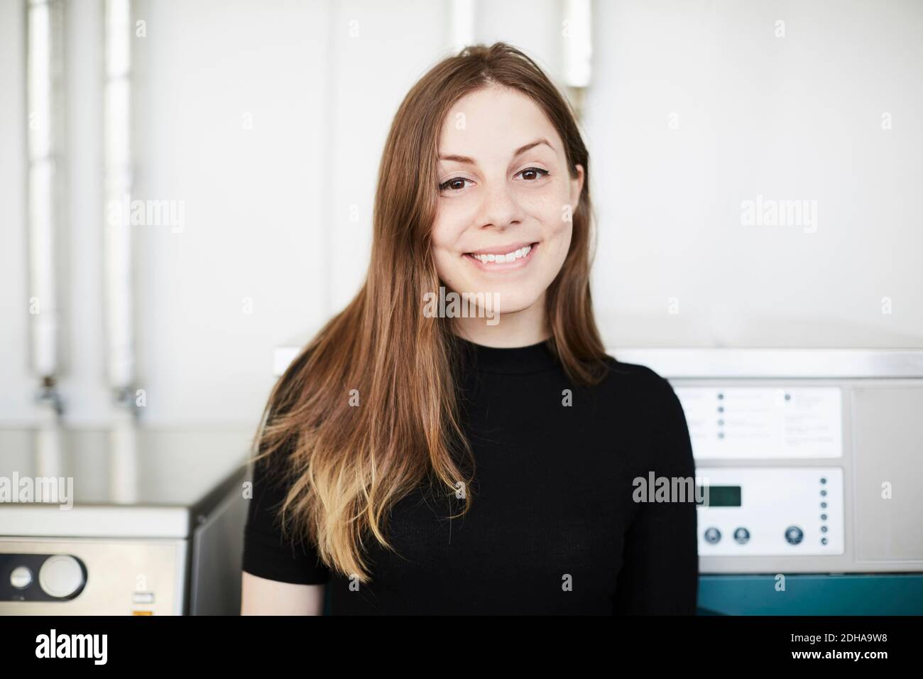 Portrait d'une jeune femme souriante avec de longs cheveux bruns debout à la laverie automatique Banque D'Images