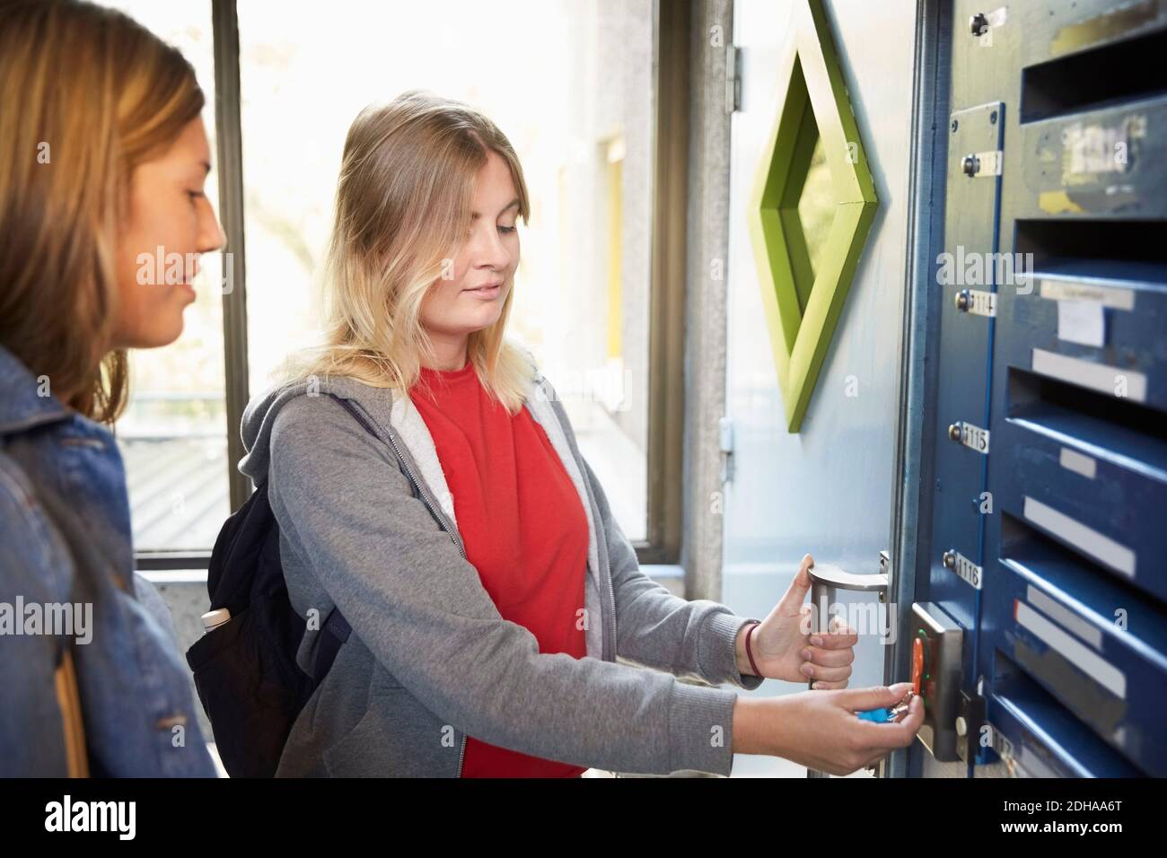 Une étudiante debout par un ami tout en déverrouillant la porte avec la clé de contact à l'université Banque D'Images