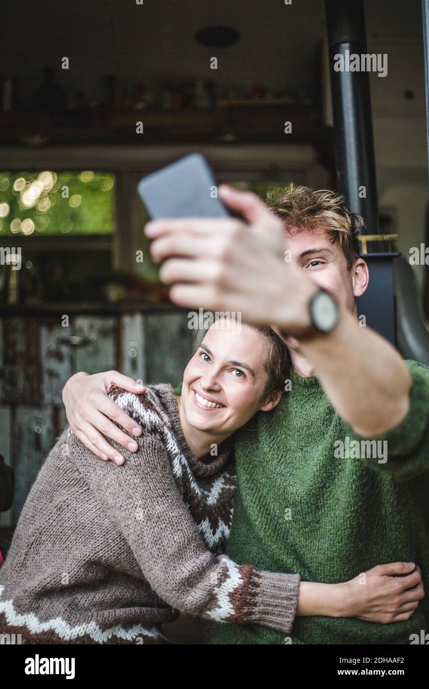Homme souriant prenant le selfie avec une femme à partir d'un téléphone portable pendant camping Banque D'Images