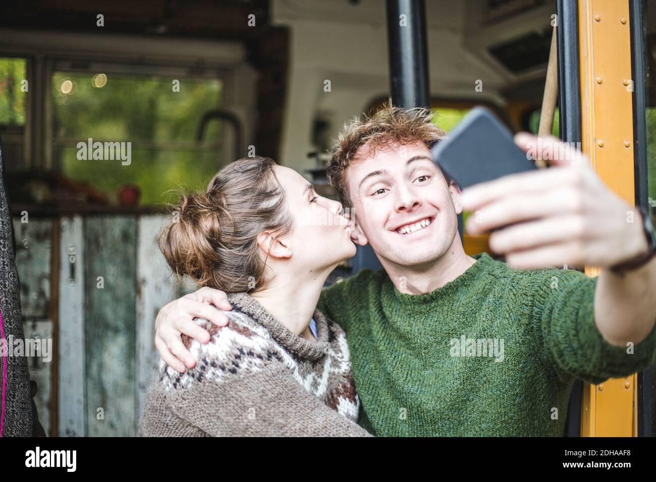 Homme souriant prenant le selfie de téléphone mobile pendant que la femme embrasse lui pendant le camping Banque D'Images