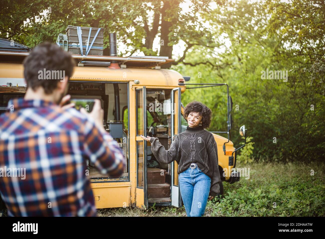 Bonne jeune femme posant contre la caravane pour petit ami pendant le camping en forêt Banque D'Images