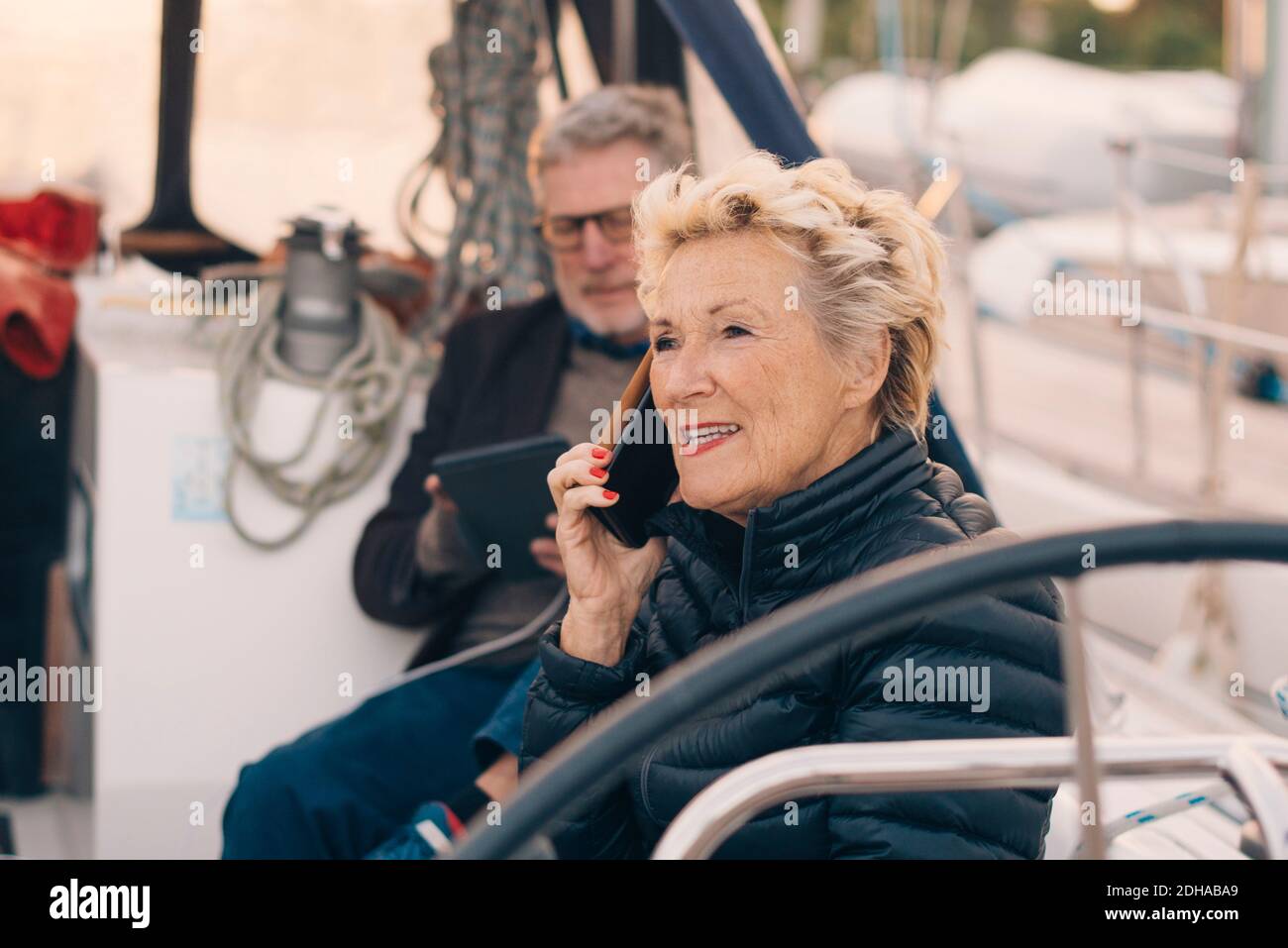 Femme âgée parlant sur un téléphone portable tout en étant assise par l'homme en yacht Banque D'Images